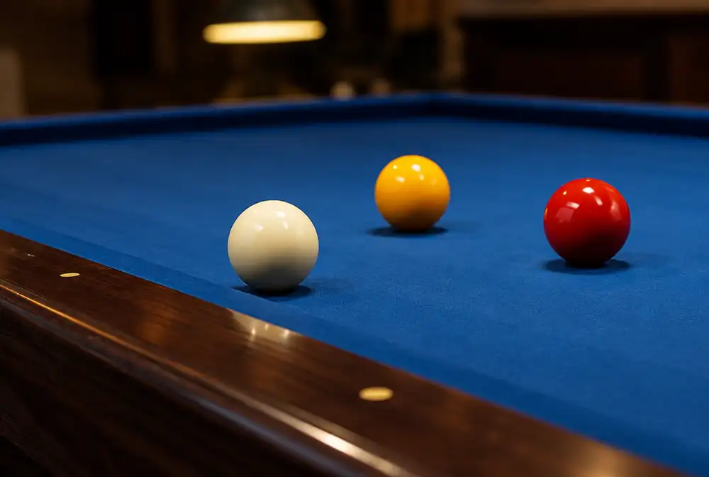 Drie caramboleballen, wit, geel en rood, op blauw laken